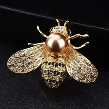 Broche abeille en métal doré avec perle marron au centre et strass noirs et blancs sur les ailes et le corps