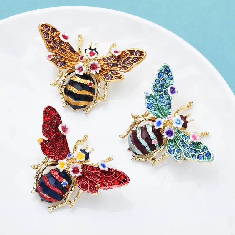 Broche abeille à fleurs en métal doré avec émail rouge, bleu et vert, détail fleurs colorées sur ailes, design élégant et finition soignée
