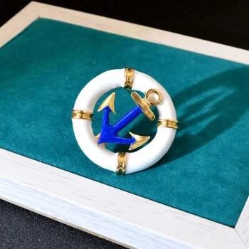 Broche ancre et bouée marine blanche avec ancre bleue et détails dorés posée sur un fond vert émeraude