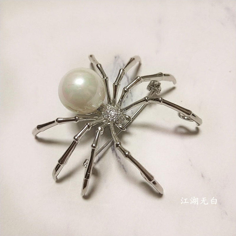 Broche araignée en métal argenté avec perle blanche et détails en strass, vue en gros plan sur le corps et les pattes