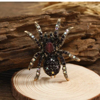 Broche araignée fantaisie noire avec strass multicolores et pierre centrale rouge sur fond bois