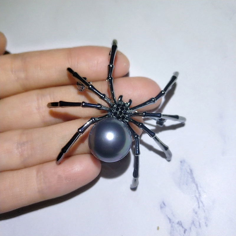 Broche araignée noire avec perle grise ronde tenue par une main