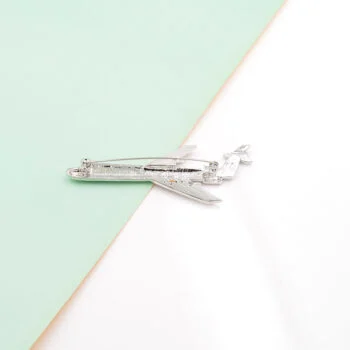 Broche avion en métal argenté avec strass vue de profil sur fond bicolore vert et blanc