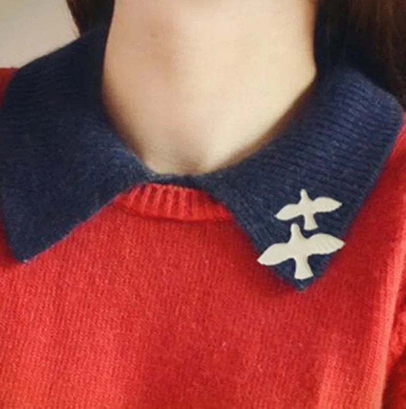 Broche blanche en forme de colombe portée sur un col en maille bleu marine