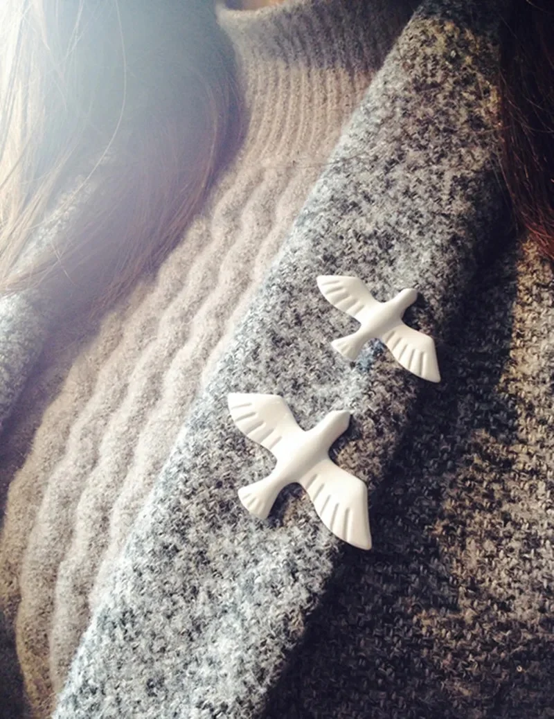 Broche blanche colombe en matière mate posée sur un manteau gris, vue rapprochée sur deux colombe stylisées avec ailes déployées