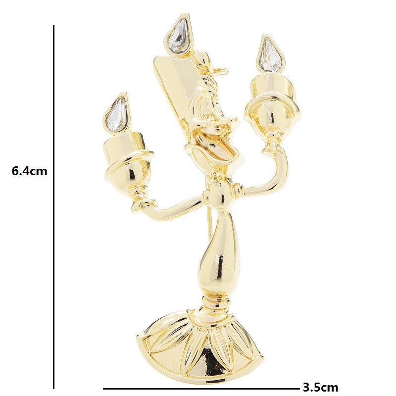 Broche bougeoir doré en métal avec trois bougies stylisées et détails en forme de goutte transparente, finition élégante et silhouette raffinée