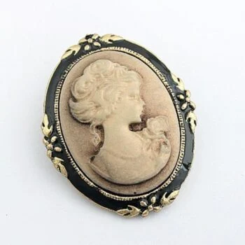 Broche camée femme de profil en résine beige sur fond noir avec cadre ovale orné de motifs floraux dorés