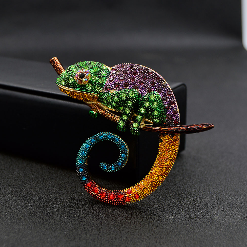 Broche caméléon coloré en métal avec strass verts, violets, jaunes, rouges et bleus, détail de queue en spirale, posé sur une branche
