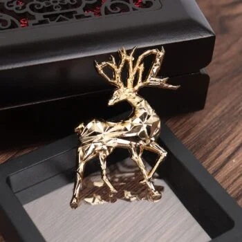 Broche cerf dorée en métal avec design facetté et détails soignés posée dans un écrin noir sur fond bois