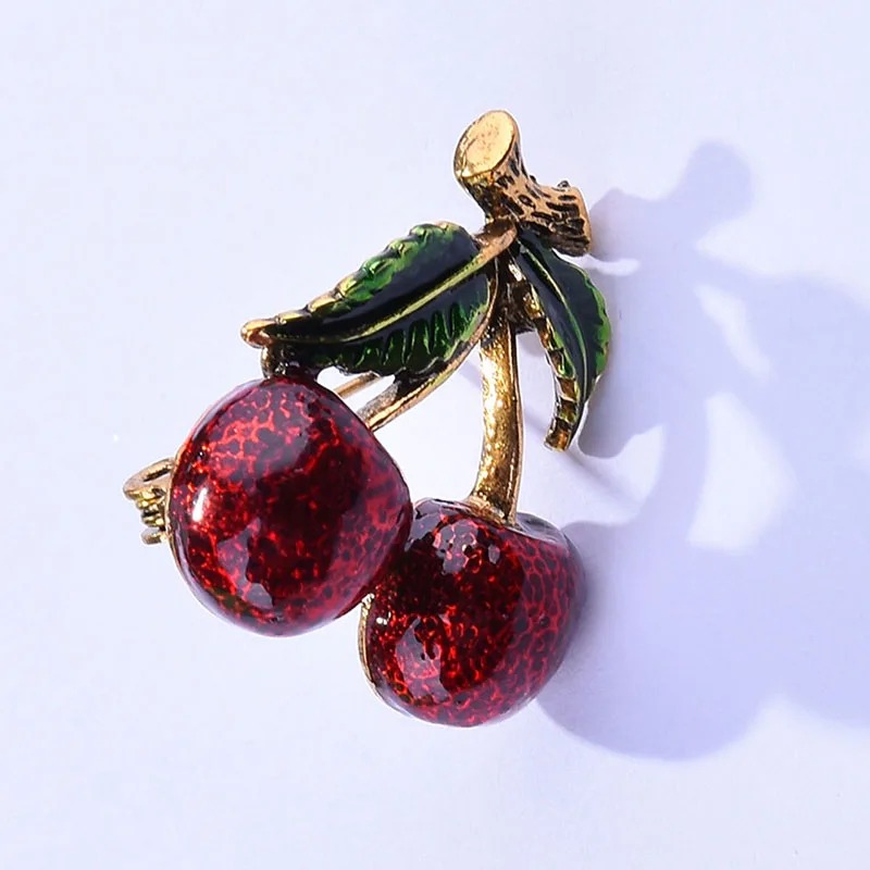 Broche cerises en métal doré avec deux fruits rouges texturés et feuilles vertes émaillées, détail soigné sur la tige