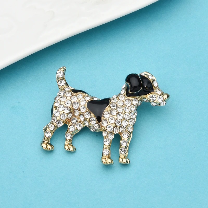 Broche chien en métal doré avec strass transparents et détails noirs, vue de face sur fond bleu