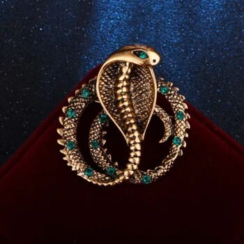 Broche cobra dorée avec yeux verts et détails turquoise sur fond rouge