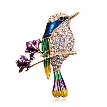 Broche colibri colorée en métal doré avec strass blancs, émail bleu, vert, violet et jaune, posée sur une branche avec feuilles violettes