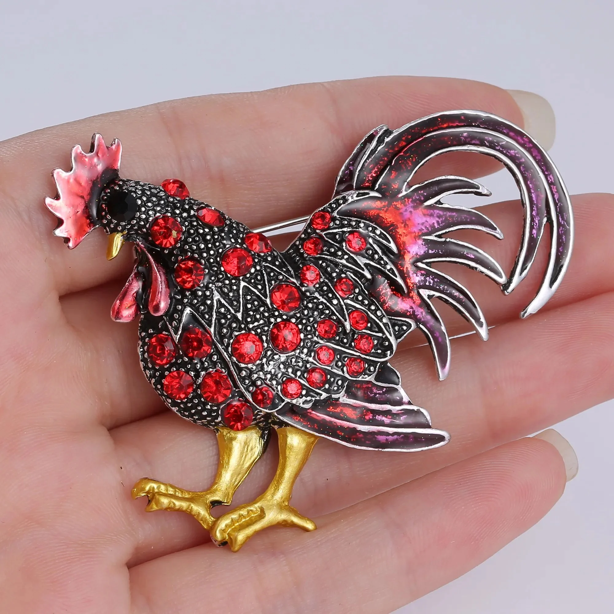 Broche Coq Fantaisie en métal argenté avec strass rouges et pattes dorées, détail du plumage travaillé et finition soignée