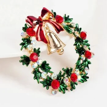 Broche couronne de Noël en métal doré avec feuillage vert, boules rouges et cloche dorée ornée d'un nœud rouge