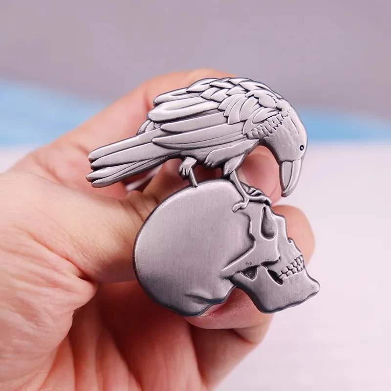 Broche en métal argenté représentant un corbeau posé sur un crâne, détail des plumes et contours sculptés