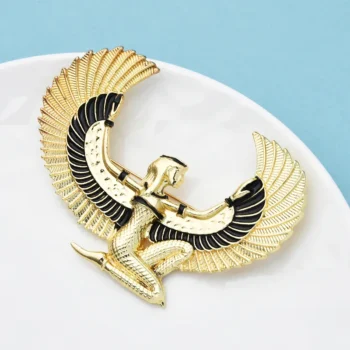 Broche déesse égyptienne Isis en métal doré avec ailes déployées et détails noirs, vue en angle légèrement de dessus