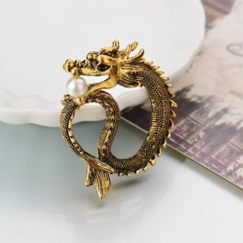 Broche dragon en métal doré avec perle blanche intégrée dans la gueule, motif détaillé et finition soignée