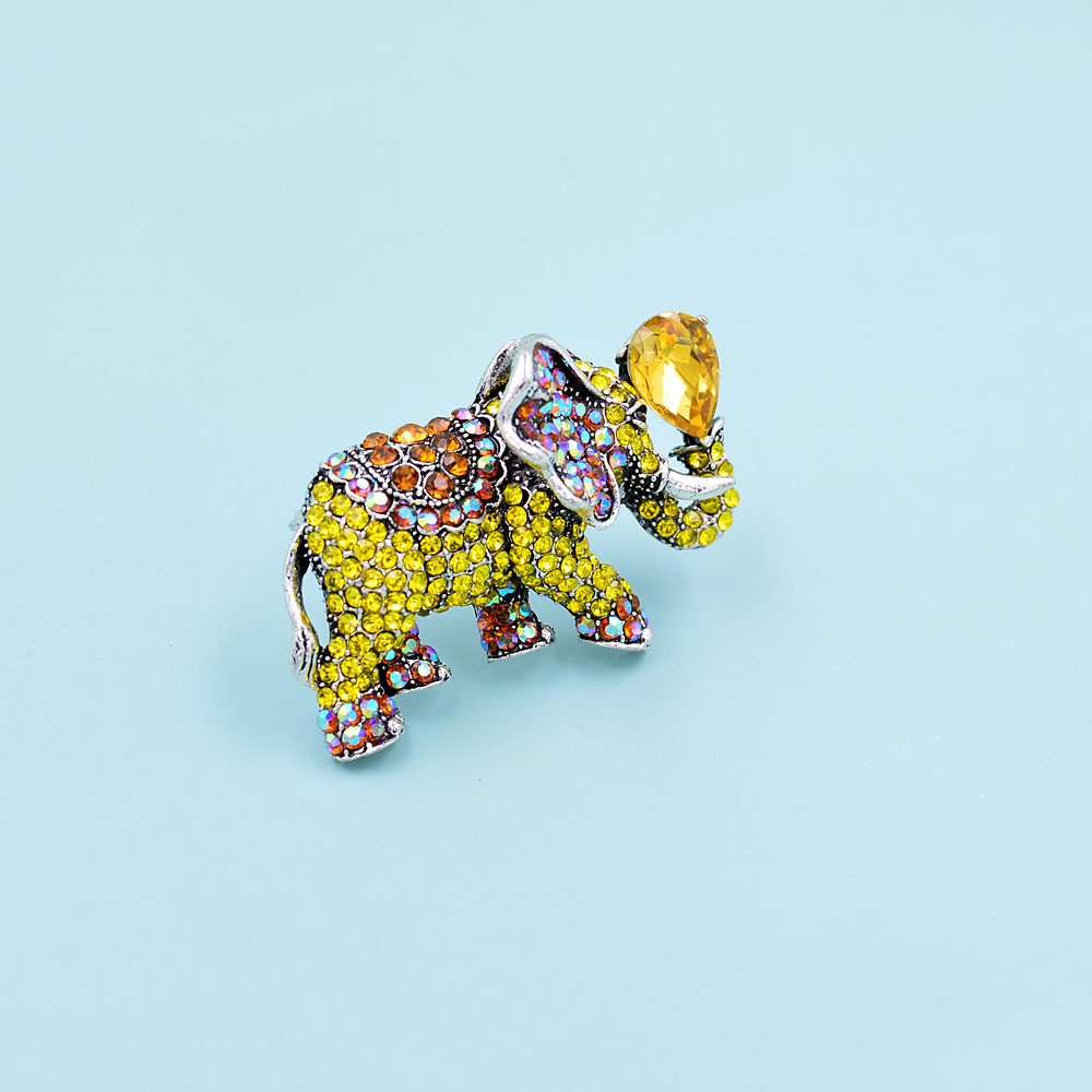 Broche éléphant fantaisie en métal argenté ornée de strass jaunes, orange et multicolores avec une pierre jaune en forme de goutte sur la trompe