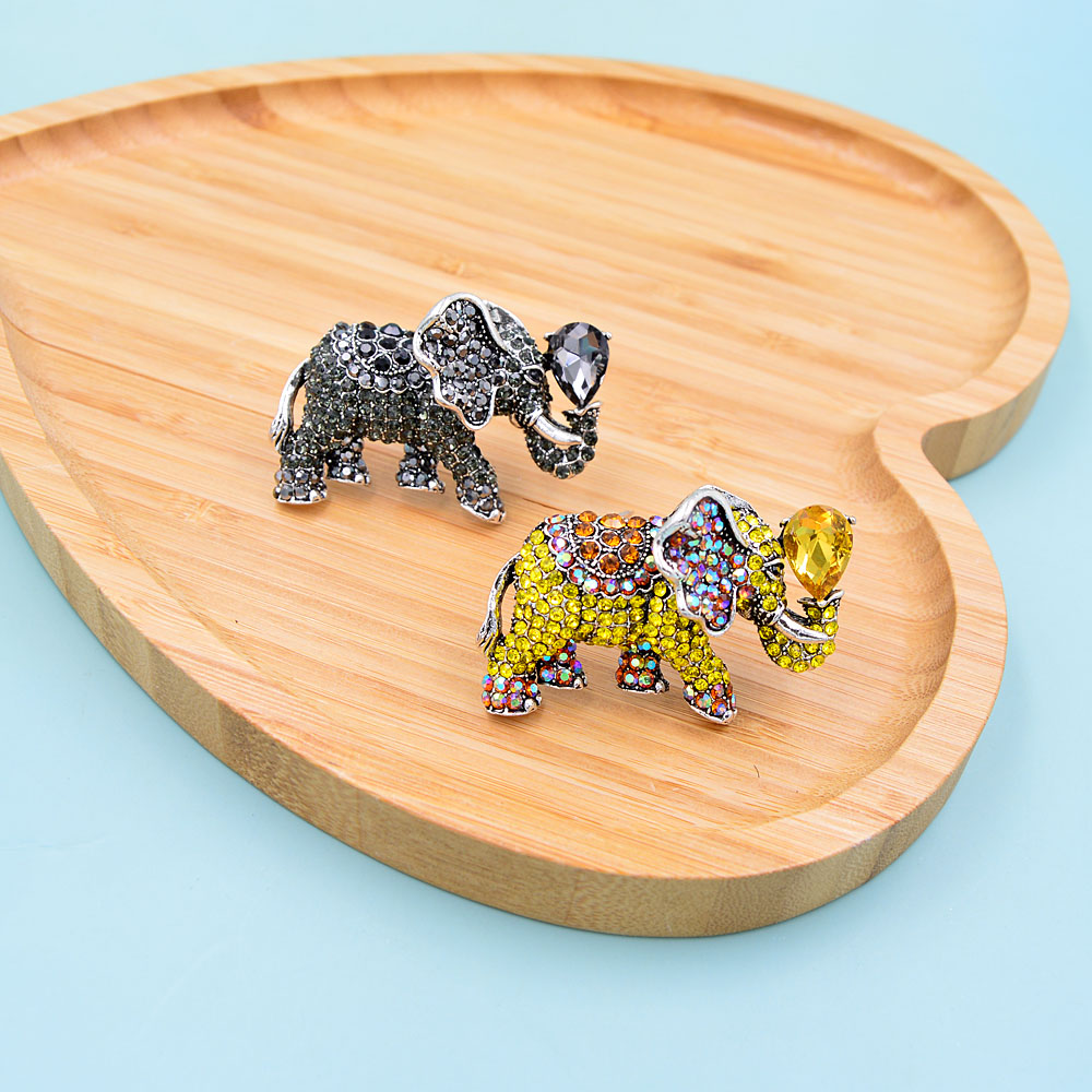 Broche éléphant fantaisie noire et broche éléphant fantaisie jaune avec strass multicolores posées sur plateau en bois clair en forme de feuille