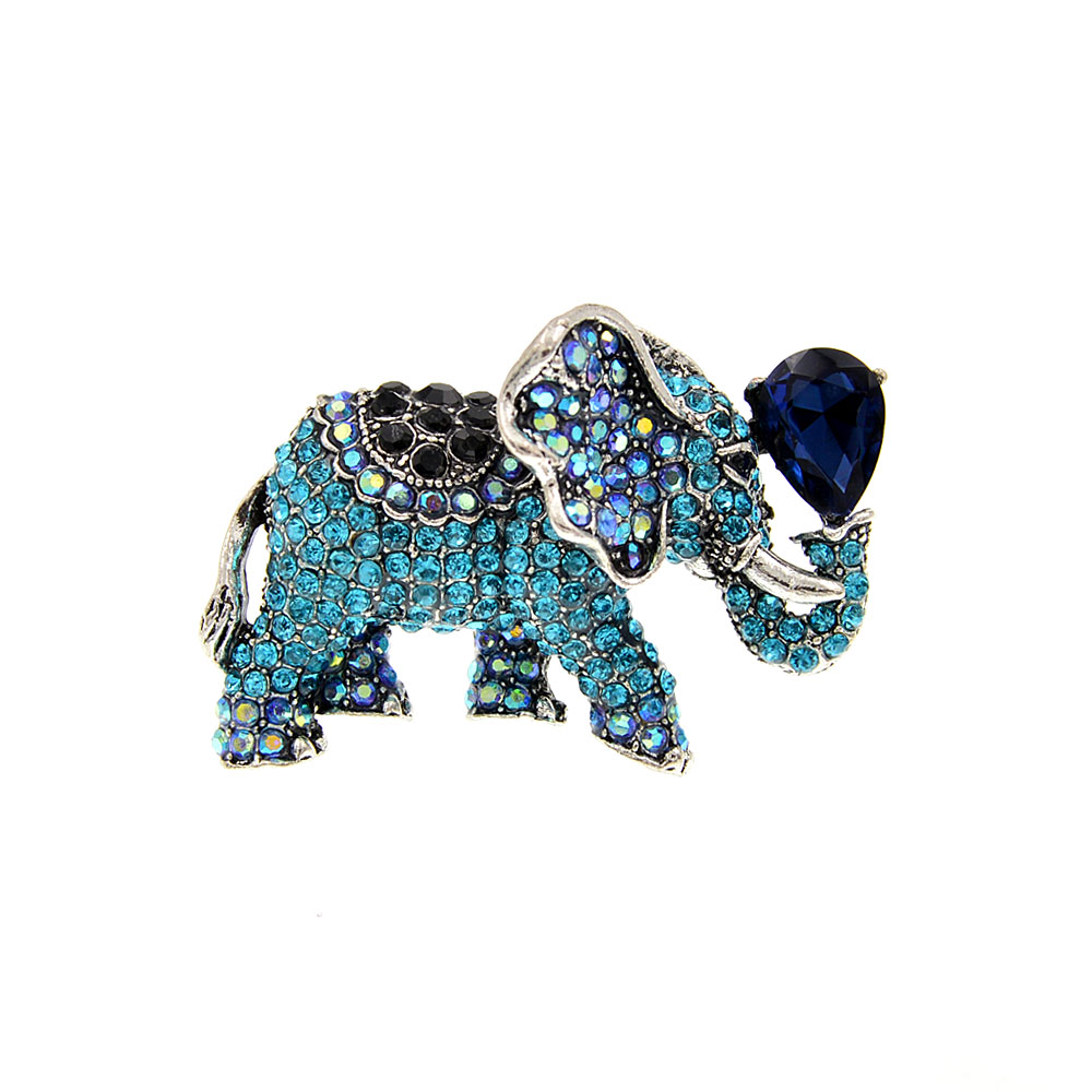 Broche éléphant fantaisie en métal argenté ornée de strass bleu clair, bleu foncé et noirs, avec une grande pierre bleue en forme de goutte tenue par la trompe
