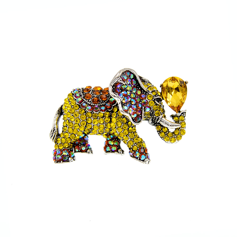Broche éléphant fantaisie en métal argenté ornée de strass jaunes, rouges et multicolores avec une pierre jaune en forme de goutte tenue par la trompe