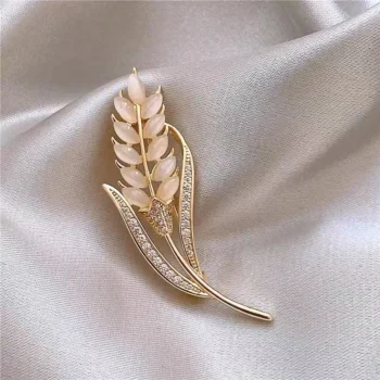 Broche feuilles élégantes en métal doré avec détails en nacre et strass, posée sur tissu satin gris clair