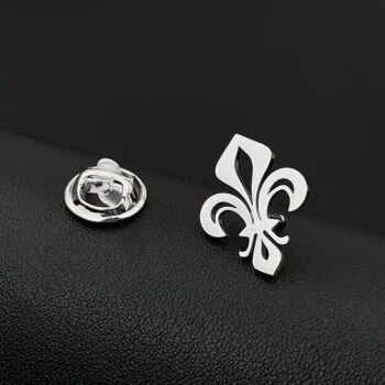 Broche Fleur De Lys en métal argenté avec motif stylisé et finition lisse posée sur surface noire