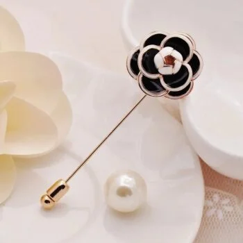 Broche fleurs de camélia noire et blanche en métal doré avec détail en émail, présentée sur fond clair avec perle et fleur décorative