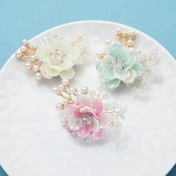 Broche fleurs et perles chic avec trois fleurs en tissu blanc, vert d'eau et rose, décorées de perles blanches et fil doré sur fond bleu clair