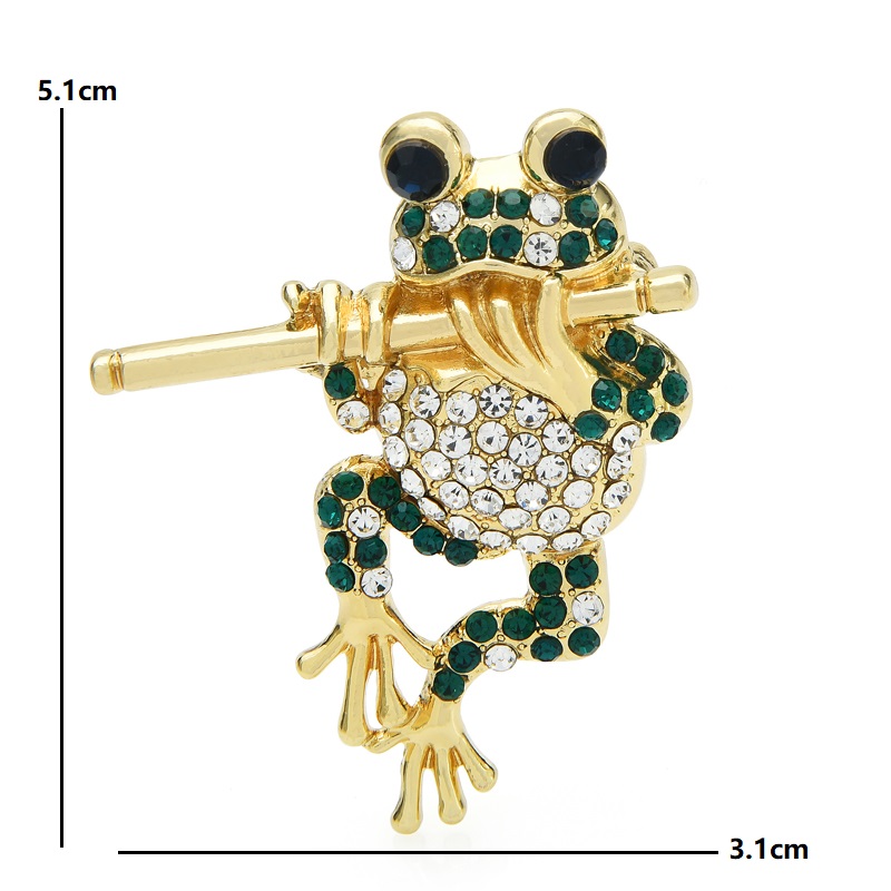 Broche grenouille dorée à la flûte ornée de strass verts et blancs, vue de face avec détails des pierres et dimensions 5,1 cm sur 3,1 cm
