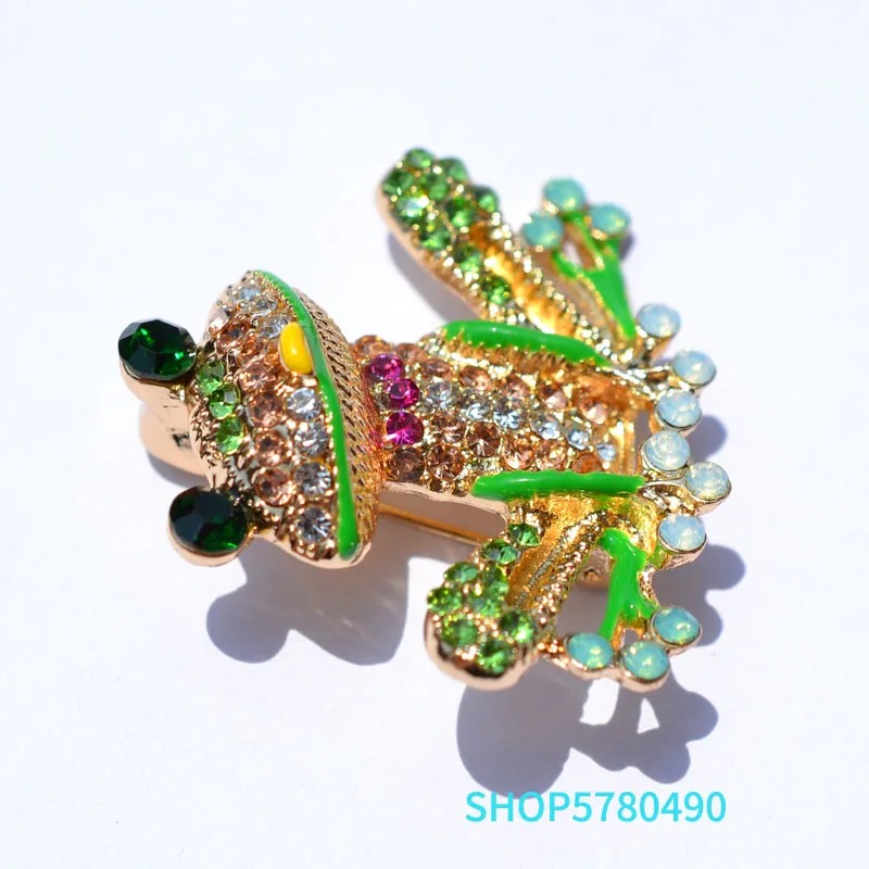 Broche grenouille originale en métal doré ornée de strass verts, roses et blancs avec détails émaillés verts et bleus