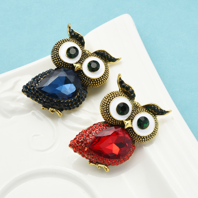 Broche hibou gros yeux avec corps en pierre facettée bleue et rouge, détails dorés et yeux blancs sur fond bleu clair