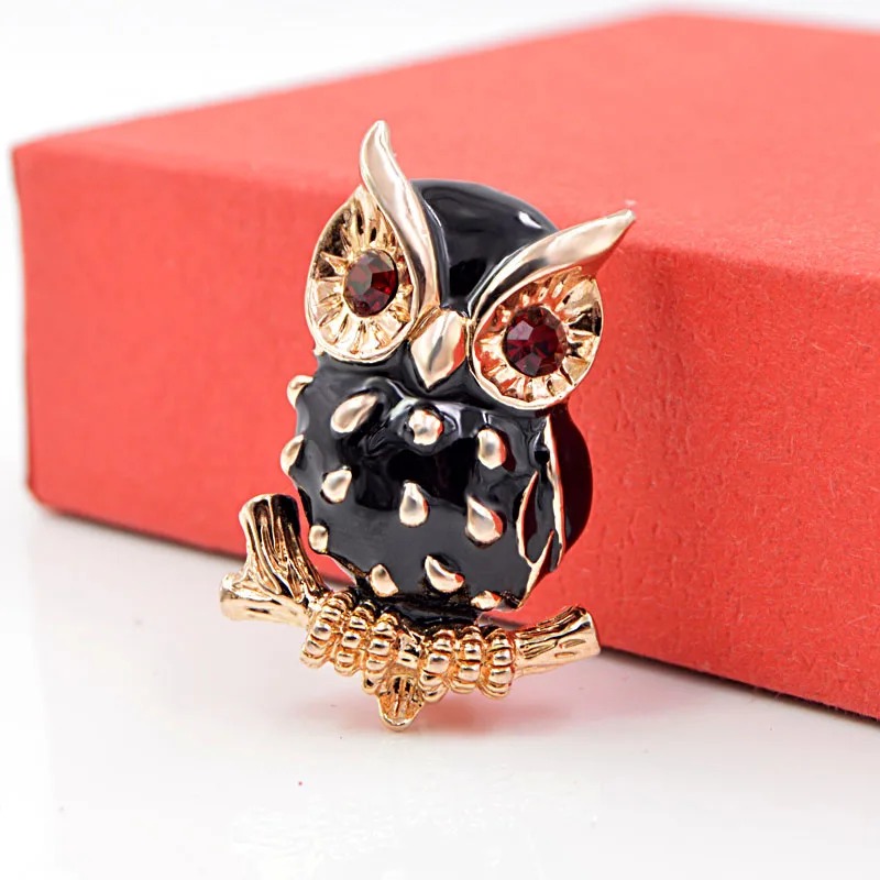 Broche hibou noir en métal doré avec yeux en pierres rouges, détail soigné sur les plumes et pose sur une branche