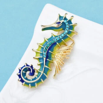 Broche hippocampe en métal doré avec émail bleu et vert, ornée de petits strass bleus sur le corps