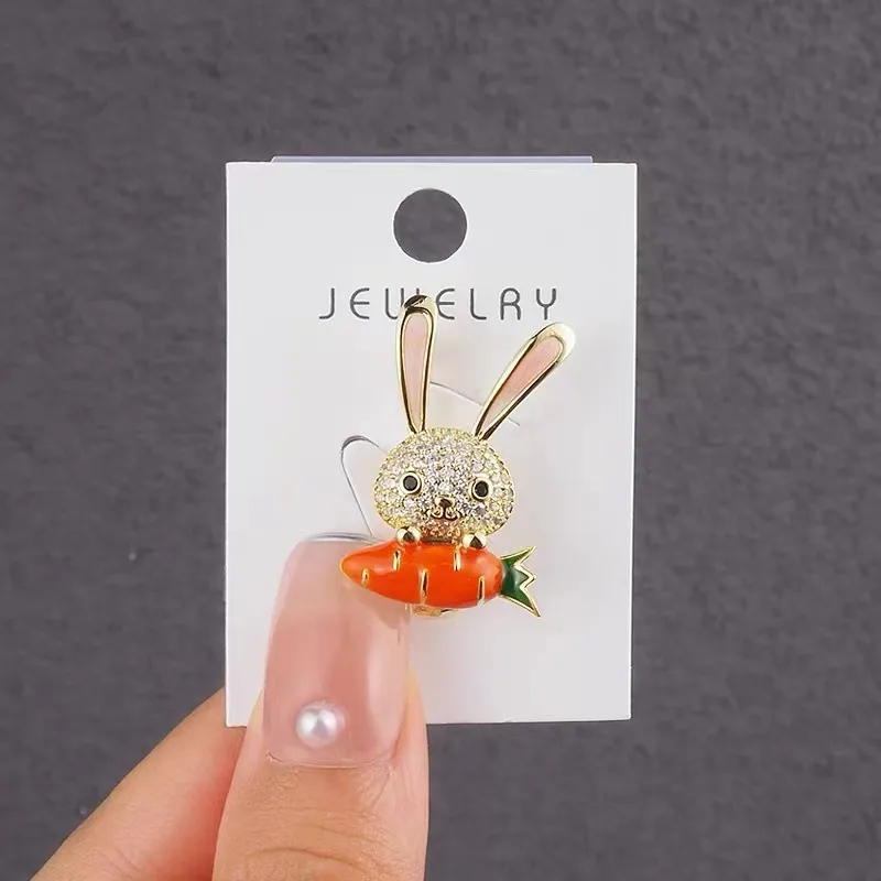 Broche lapin en strass avec carotte orange tenue devant fond gris