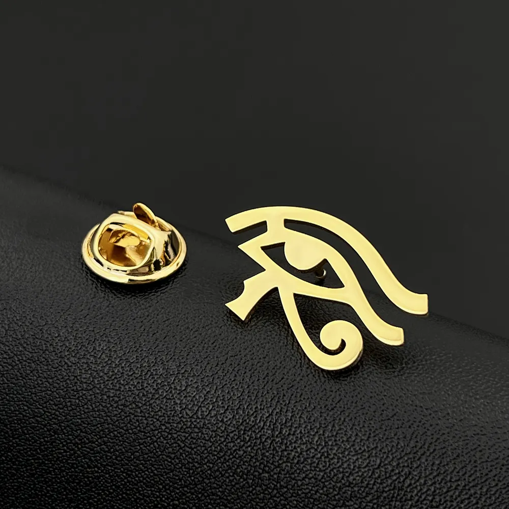 Broche œil d'horus en métal doré avec attache papillon posée sur surface noire