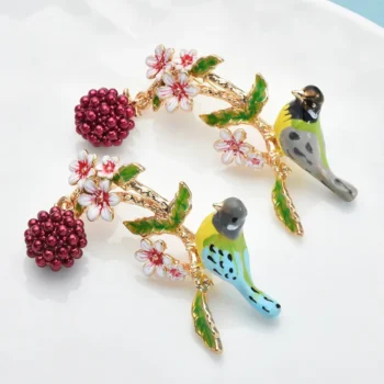 Broche oiseau sur branche fleurie avec fleurs blanches, feuilles vertes et baies rouges en émail et métal doré, détail soigné