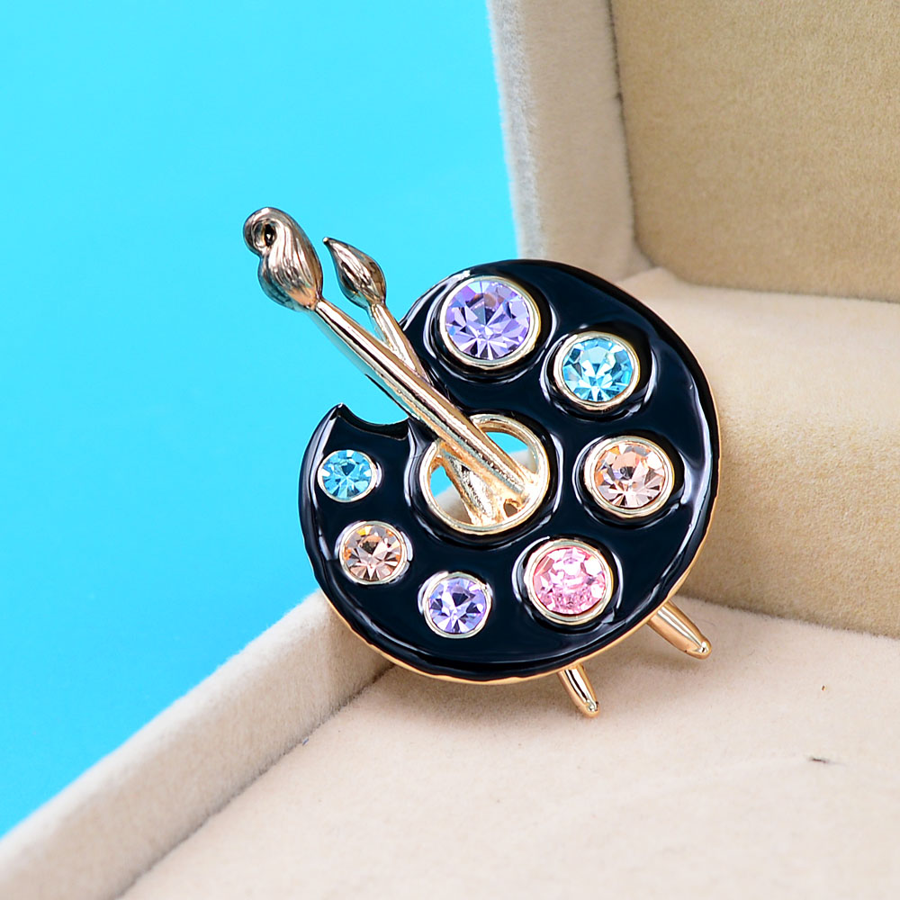 Broche palette de peintre en métal doré avec émail noir et strass colorés bleu, violet, rose et beige, détail pinceau