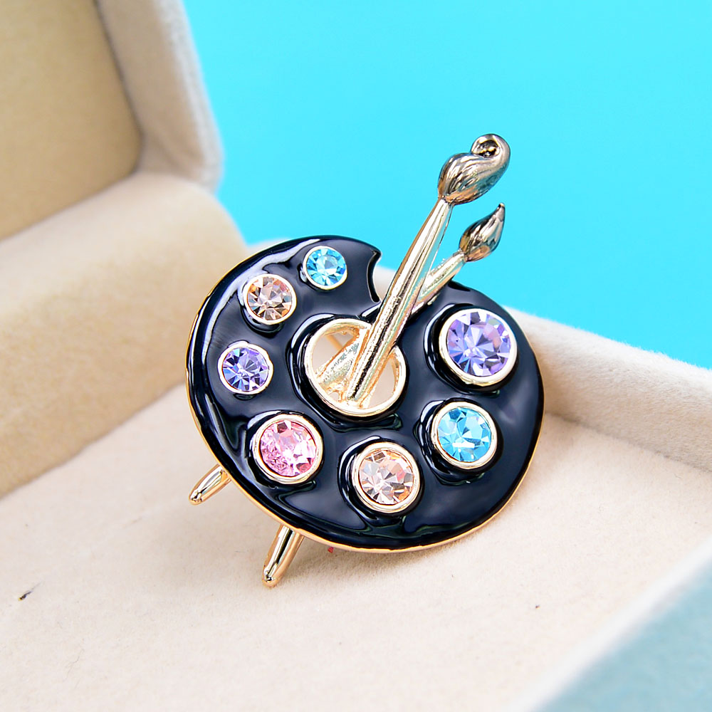Broche palette de peintre noire en métal doré avec strass colorés et pinceaux détaillés