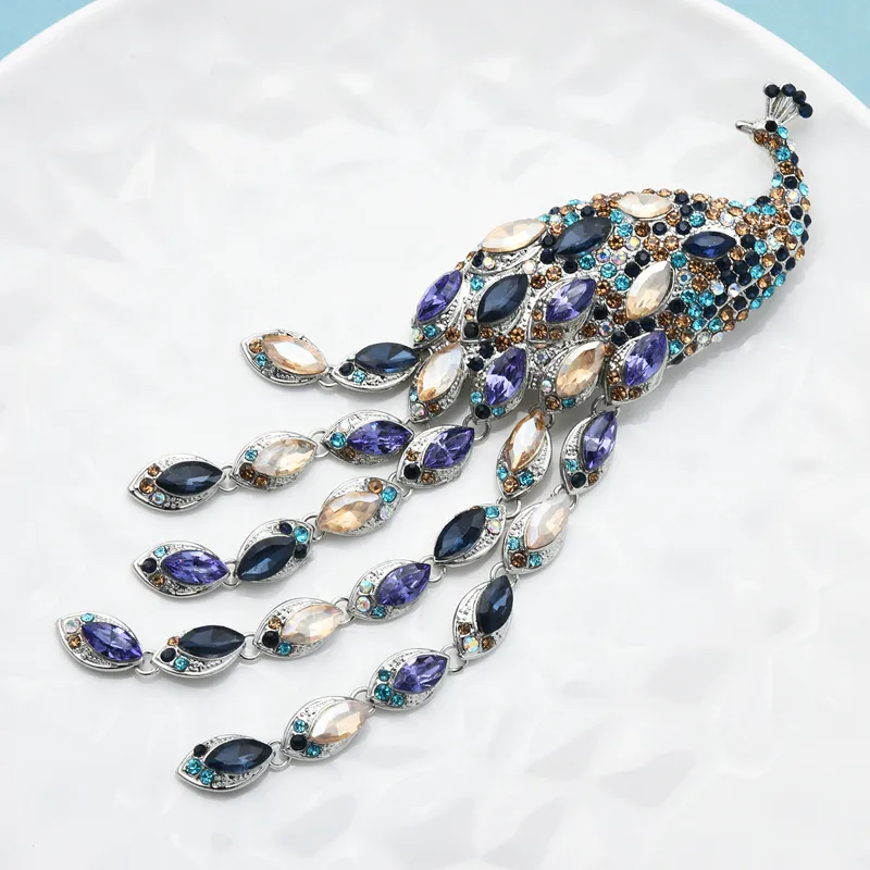 Broche paon femme avec plumes pendantes en pierres bleues, violettes et blanches, finition soignée en métal doré
