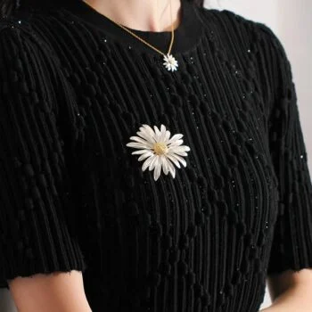 Broche Pâquerette blanche en forme de fleur avec détail soigné portée sur un haut noir texturé