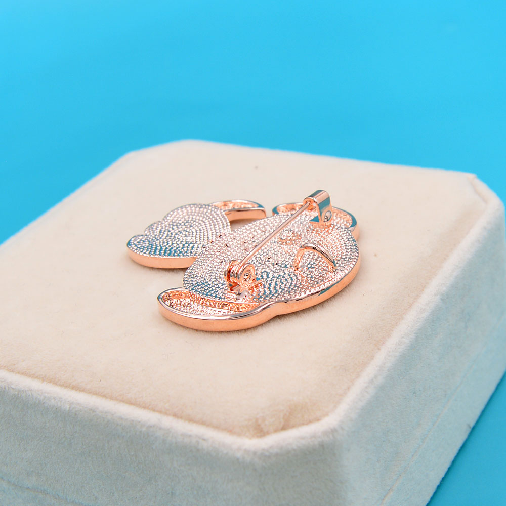 Broche petit chien en métal doré rose avec strass, vue en léger angle sur un coussin beige