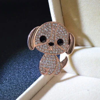 Broche petit chien en métal doré rose orné de strass blancs avec yeux noirs, posée dans un écrin beige