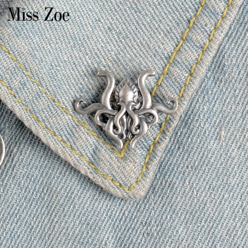 Broche pieuvre en métal argenté fixée sur un col de veste en jean bleu clair avec couture jaune