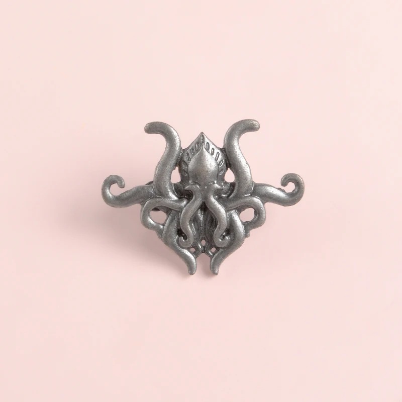 Broche pieuvre en métal argenté vue de face sur fond rose clair