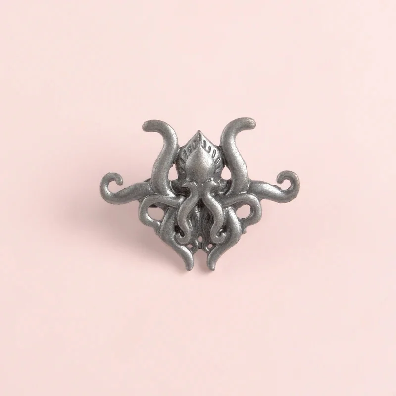 Broche pieuvre en métal argenté vue de face sur fond rose clair