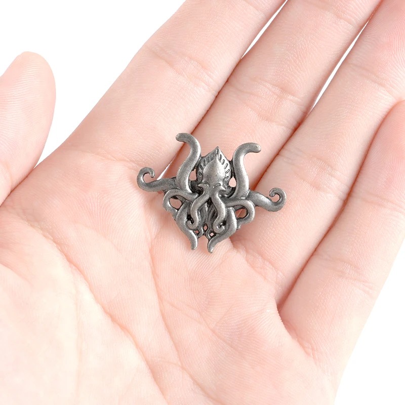 Broche pieuvre en métal gris foncé tenue dans la paume d'une main, montrant le design détaillé des tentacules enroulées