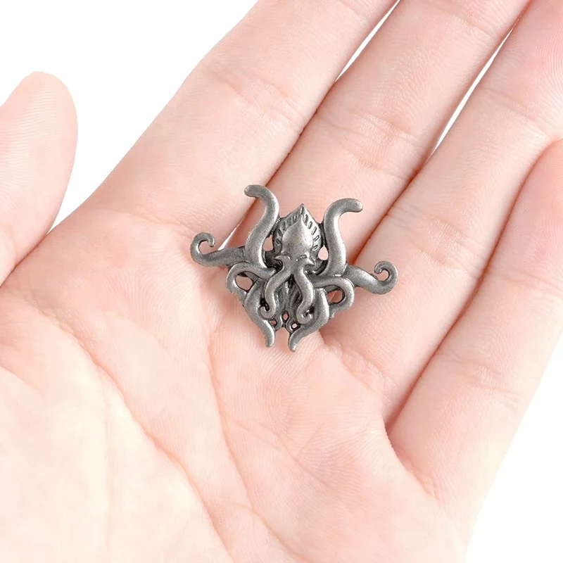 Broche pieuvre en métal gris foncé tenue dans la paume d'une main, montrant le design détaillé des tentacules enroulées