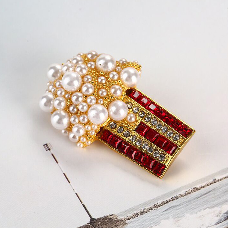 Broche Pop Corn Fantaisie dorée ornée de perles blanches et de strass rouges et transparents, vue en léger angle